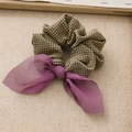 Detalle de un coletero de tela a cuadros con un lazo de gasa morada sobre fondo beige - Verde Púrpura Profundo