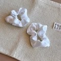 Dettaglio di due eleganti elastici scrunchie in raso bianco su superficie tessuta - Pezzo Singolo / Bianco Piccolo