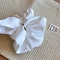 Primo piano di un grande scrunchie in seta bianca con pieghe morbide su sfondo in tessuto - Pezzo Singolo / Bianco Grande