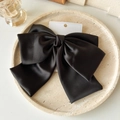 Detail einer großen schwarzen Satin-Schleifen-Haarklammer auf einer Steinplatte - Schwarz