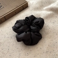 Elegant black satin scrunchie detail on beige knit fabric with decorative book - Black