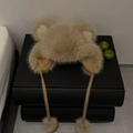 Dettaglio cappello di peluche con orecchie da orso e lacci con pompon decorativi - Cachi