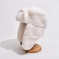 Winter thermal plush earflap hat in creamy white faux fur on a wooden display stand - One Size / Off White