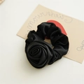 Detailopname van een handgemaakte zwarte satijnen scrunchie met een grote 3D-roosvorm - Roos Zwart