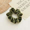 Primo piano di un elastico per capelli in velluto verde scuro con morbide pieghe - Verde