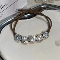 Close-up of brown elastic hair tie featuring five sparkling round rhinestones on a tray - Brown