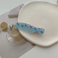 Gros plan d'un peigne à cheveux bleu clair ondulé avec des motifs floraux rouges sur plateau - Bleu