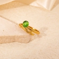 Detalle de anillo de serpiente dorado con gema verde sobre piedra beige y fondo de satén - Estilo Serpiente Piedra Verde (R0729)