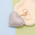 Macro detail of a grey heart-shaped PU leather keychain on a beige tray with gold hardware - Gold Chain Clasp / Silver