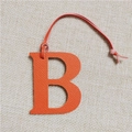Detail of orange lychee textured leather letter B bag charm on beige linen background - Letter B Orange