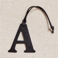 Close-up of black lychee leather A-letter bag charm on a soft beige linen background - Letter A Black