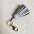 Detailed close-up of grey leather tassel keychain with polished gold metal hardware - Gray