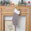 Calza natalizia in maglia grigia appesa a un camino in legno con decorazioni festive - Grigio
