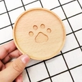 Round wooden coaster with paw print cutout design shown being held by hand - Beech Wood Little Bear Paw 10cm