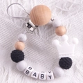 Detail of wooden baby pacifier clip with silicone beads and crown pendant on knit fabric - White