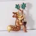 Detail of an enamel squirrel brooch with acorns and green leaves on a white box - Brown