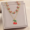 Elegant gold layered cherry necklace with vibrant red fruit charms on a jewelry box - Cherry Style