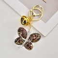 Dettaglio di una farfalla nera glitterata con campanellino dorato su un portachiavi - Chiusura Oro Chiaro + Farfalla + Campanellino / Oro Grigio