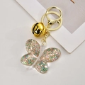 Close-up of a clear acrylic butterfly keychain filled with colorful glitter and gold flakes - Light Gold Clasp + Butterfly + Bell / Orange Green