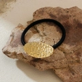 Golden hammered metal oval ponytail holder with black elastic band on natural rock - Gold Hammered Oval Style