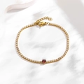 Detail of gold tennis bracelet featuring white zircons and a central red round gemstone - Round Red Zirconia