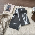 Flat lay of a grey knit scarf with white patterns, magazine and coffee pot on white fur - Scarf-Gray