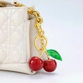 Sparkly red cherry bag charm with green leaves on white quilted handbag detail - Red Cherry with Leaf