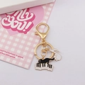 Portachiavi gatto su pianoforte dorato con ciondolo nota musicale su sfondo rosa - Gatto al pianoforte con zampa bianca