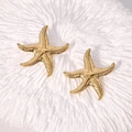 Golden starfish earrings with hammered texture on a white coral background - Gold