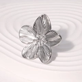 Elegant silver flower ring with textured petals on a minimalist white pedestal base - Steel