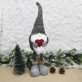 Nordic Christmas gnome with knitted hat and red heart on snow and pine cones background - Gray