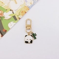Dettaglio di un portachiavi con panda e bambù dorati su uno sfondo bianco pulito - Panda frontale che tiene il bambù