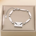 Detail view of silver envelope bracelet with zircons and K18 tag on a jewelry box - Envelope Style / Silver (KB180777-SP)