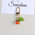 Detail view of a glass persimmon keychain with a green leaf and golden metal clasp - Translucent Persimmon Pendant