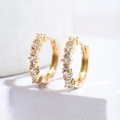 Dettaglio di orecchini a cerchio dorati con zircone blu su sfondo bianco minimalista - Zirconia Bianca / Oro