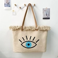 Detail view of canvas tote bag with embroidered evil eye pattern and beige fringe tassels - Blue Eye with Lashes
