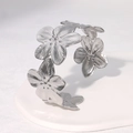 Minimalist silver stainless steel open bangle with 3D floral design on white stand - Steel
