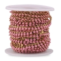 Macro detail of pink enamel beads and gold stainless steel chain on white spool - Pink