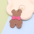 Detail of a brown leather-texture bear keychain with a pink bow and golden metal ring - Keychain style / Bear with Bow