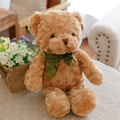 Oso de peluche marrón con un lazo de cinta verde sentado en un sofá acogedor - Oso Con Lazo Bronceado