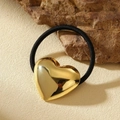Dettaglio di un ciondolo a cuore dorato su un elastico per capelli nero su pietra - Stile Cuore Oro