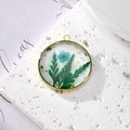 Detailed close-up of a gold metal frame pendant with blue dried flowers and gold leaf - March Blue Flower With Green Leaves And Gold Foil
