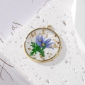 Macro shot of a round copper frame pendant with real blue dried flowers and gold foil accents - Gold Foil Multi-leaf Blue Flower