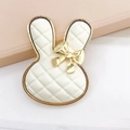 Detailed macro view of a white rabbit-shaped accessory with gold trim and plaid pattern - Off-white