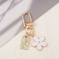 Macro shot of gold metal keychain with a white flower charm and Hand Made engraved tag - White