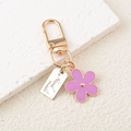 Dettaglio di ciondolo a fiore in smalto viola e moschettone dorato con targhetta handmade - Viola