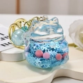 Macro shot of liquid glitter lucky cat keychain with blue fluid and pink pearls inside - Blue