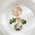 Close-up of panda and bamboo enamel pendants with gold-plated keychain on white plush base - Panda Eating Bamboo