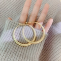 Dettaglio ravvicinato di grandi orecchini a cerchio dorati tenuti su uno sfondo in maglia - Oro Opaco Cerchio (Perno in Argento)