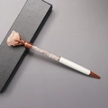 Detail van een witte metalen pen met roze kristalfragmenten en ruwe steen in geschenkdoos - Rozenkwarts